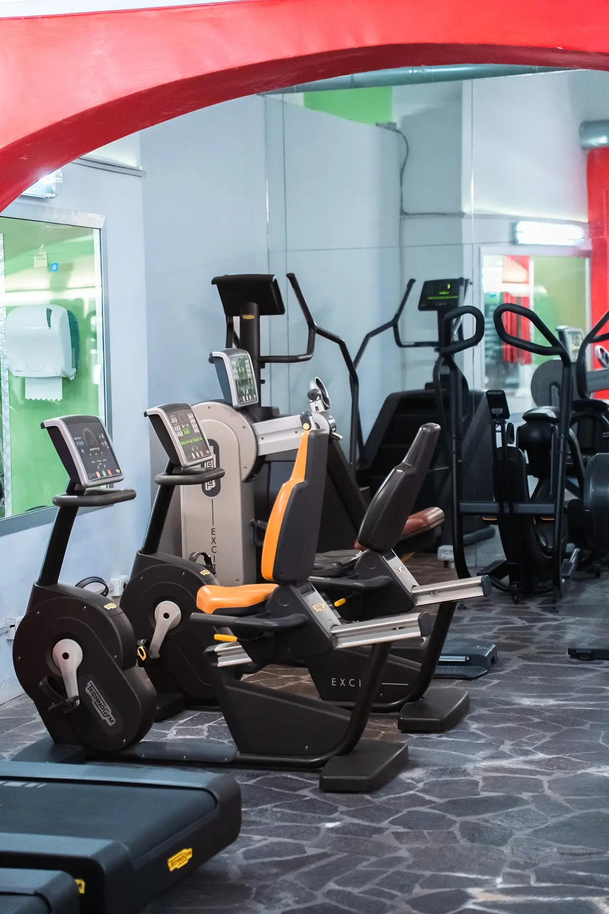 Cardio: Bike, ellittiche e tapis roulant sotto l’arco rosso.